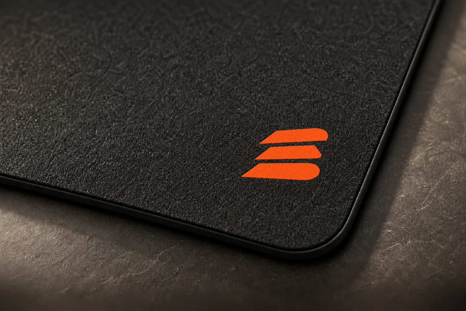 Charcoal Buildside mouse pad with an orange stacks mark beside a laptop, close-up view
